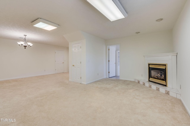 unfurnished living room featuring a glass covered fireplace, a notable chandelier, baseboards, and light carpet