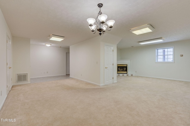 below grade area with visible vents, a notable chandelier, a textured ceiling, a fireplace, and light colored carpet