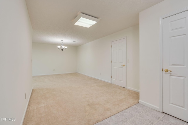 spare room with light carpet, a notable chandelier, a textured ceiling, and baseboards