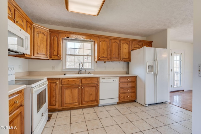 kitchen with light countertops, brown cabinetry, white appliances, a textured ceiling, and a sink