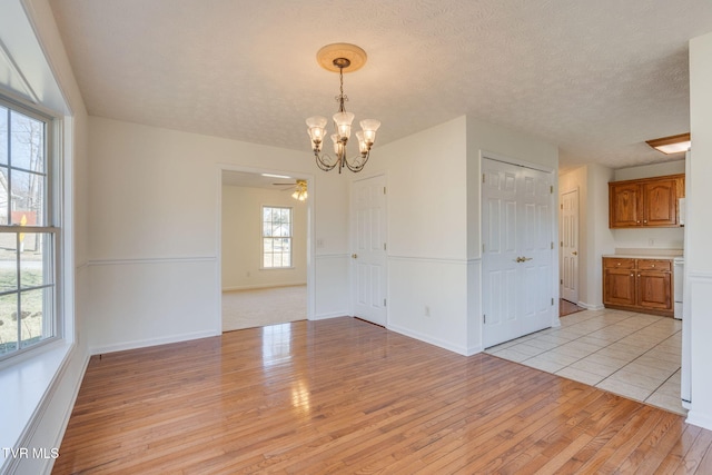 unfurnished dining area with baseboards, a textured ceiling, an inviting chandelier, and light wood-style flooring