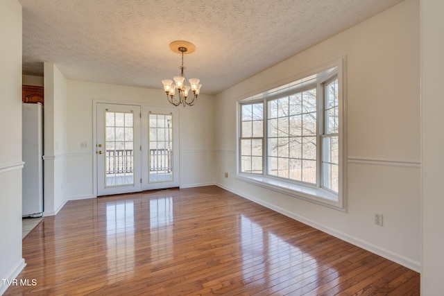 unfurnished room with a textured ceiling, baseboards, wood-type flooring, and a chandelier