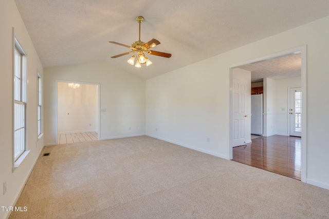 empty room with visible vents, ceiling fan with notable chandelier, a textured ceiling, carpet, and lofted ceiling