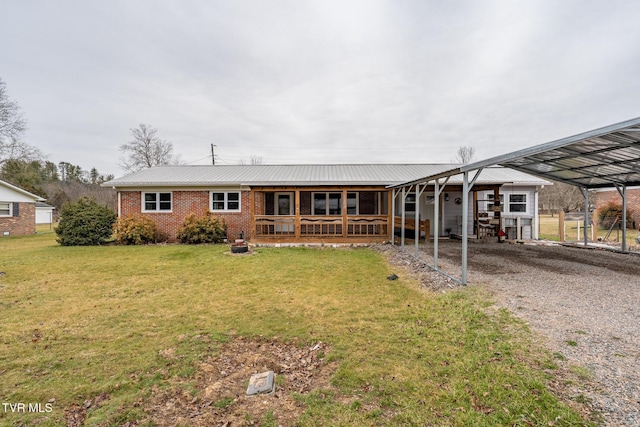 back of property featuring a yard, brick siding, driveway, and metal roof