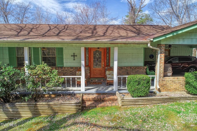 entrance to property featuring brick siding, covered porch, and roof with shingles