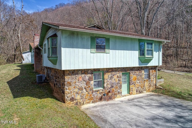 view of side of property with stone siding, a forest view, central AC, and a yard