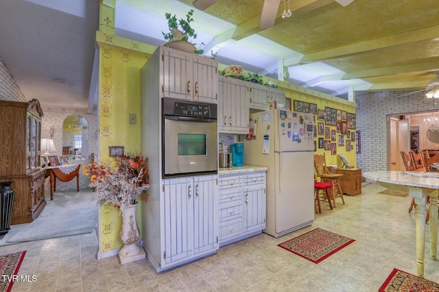 kitchen featuring light floors, brick wall, freestanding refrigerator, oven, and light countertops