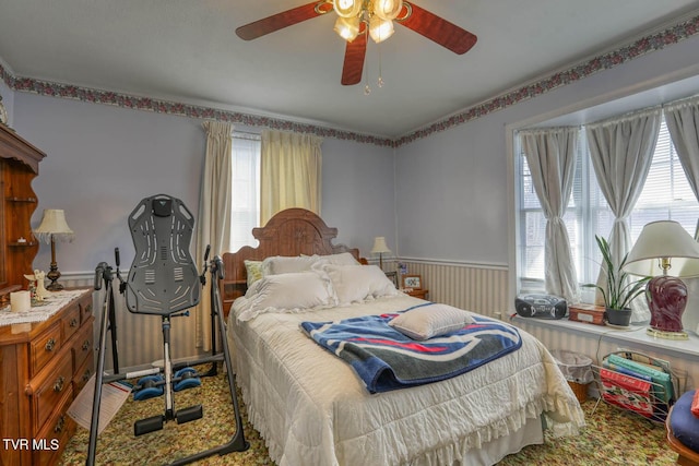 bedroom with a ceiling fan and a wainscoted wall