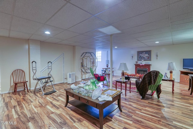 living area with light wood-style flooring, a fireplace, baseboards, and a paneled ceiling