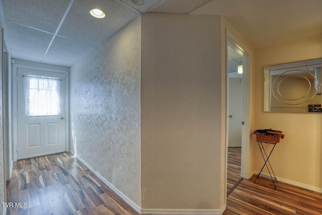 corridor with wood finished floors, a paneled ceiling, baseboards, and a textured wall