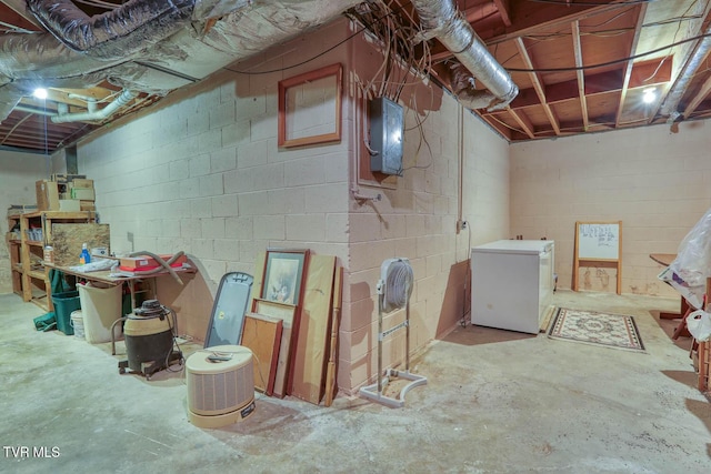 unfinished below grade area featuring fridge, concrete block wall, and electric panel