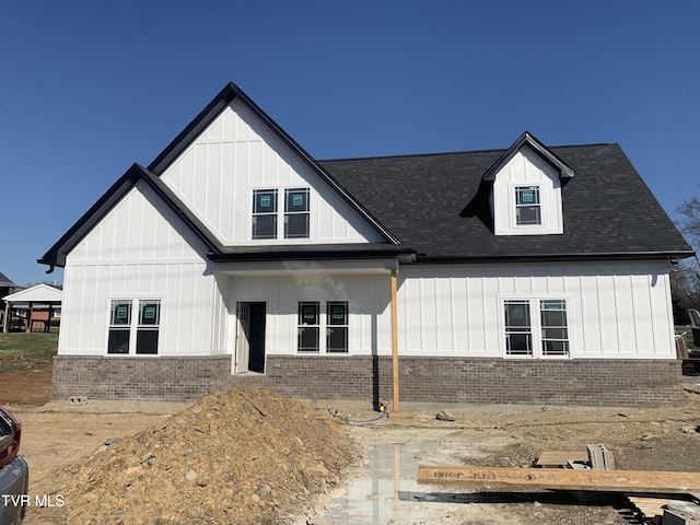 modern farmhouse with board and batten siding, brick siding, and a shingled roof