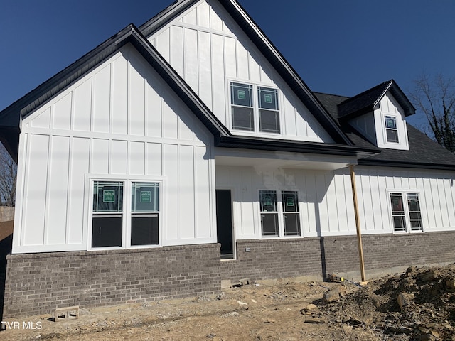 view of side of home with brick siding, board and batten siding, and roof with shingles