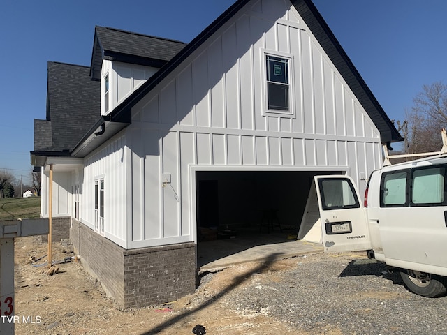 view of side of home with roof with shingles, board and batten siding, and an attached garage