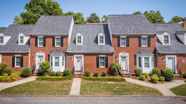 multi unit property with a front lawn, brick siding, and roof with shingles