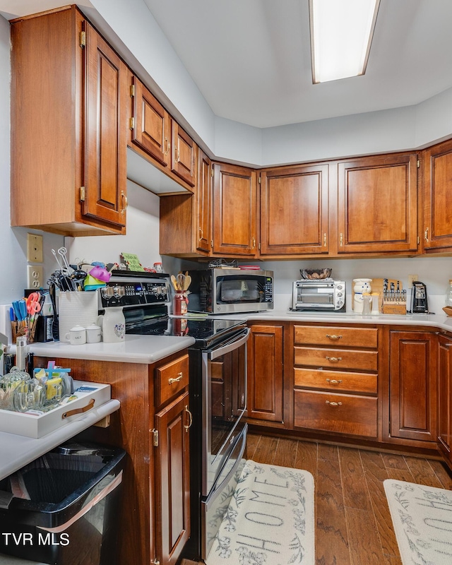 kitchen featuring stainless steel appliances, dark wood-style floors, brown cabinetry, and light countertops