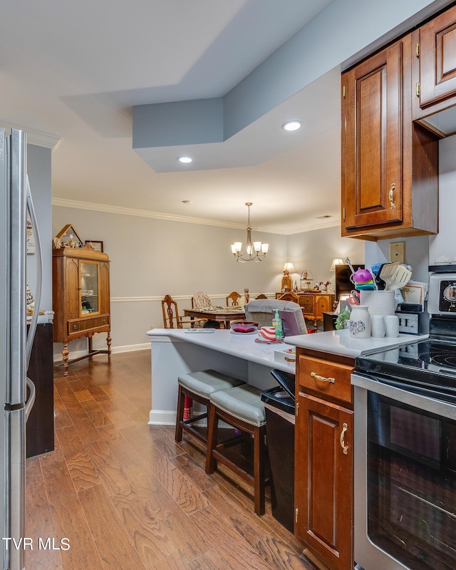 kitchen featuring light countertops, ornamental molding, brown cabinets, wood finished floors, and stainless steel appliances