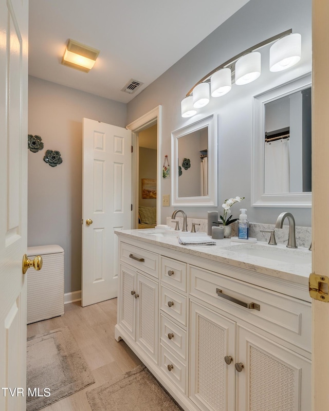 bathroom with double vanity, wood finished floors, visible vents, and a sink