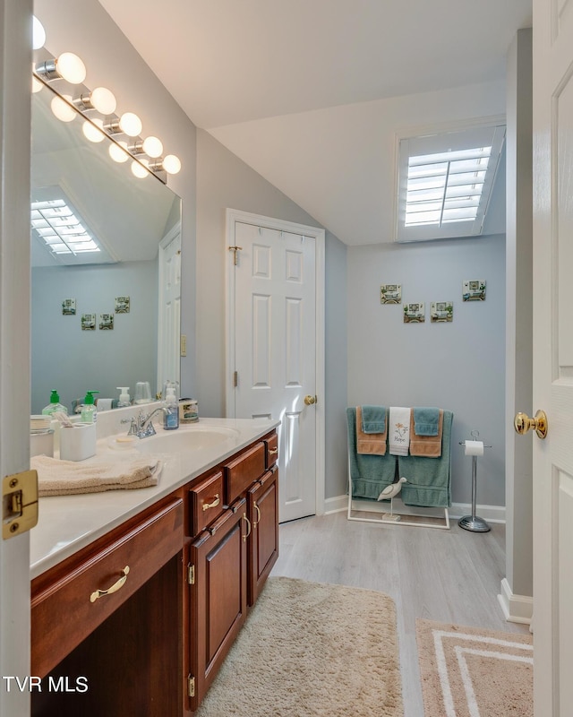 bathroom with vanity, lofted ceiling, wood finished floors, and baseboards