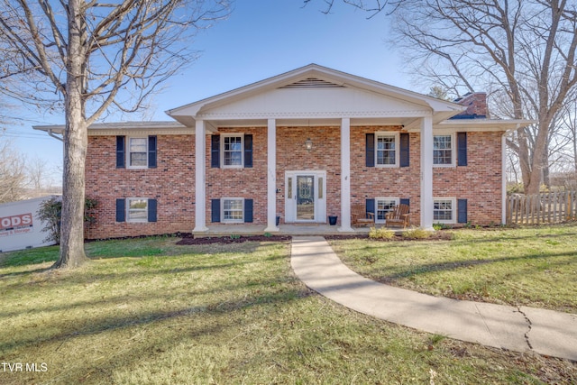 view of front of house with fence, a porch, a chimney, a front lawn, and brick siding