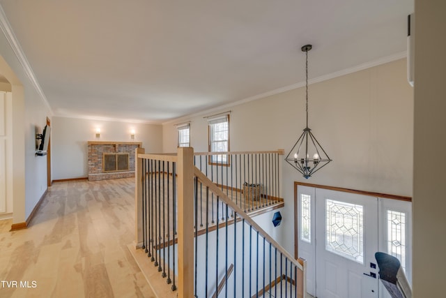 entryway featuring ornamental molding, an inviting chandelier, light wood finished floors, baseboards, and a brick fireplace