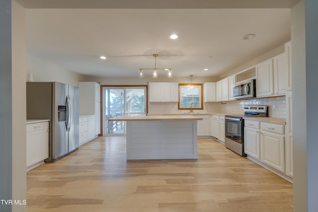 kitchen with light wood-type flooring, light countertops, appliances with stainless steel finishes, white cabinetry, and a sink