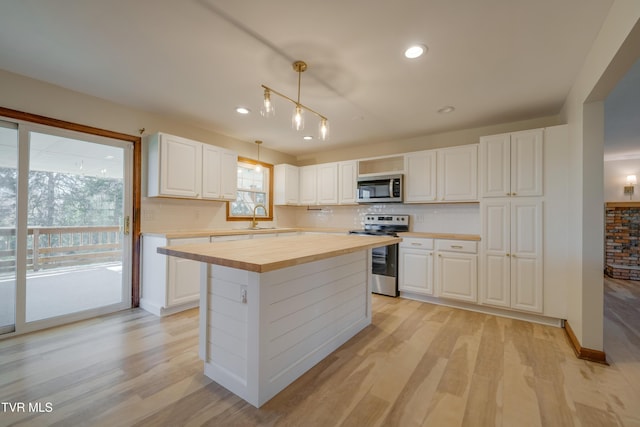 kitchen with light wood-style flooring, a sink, appliances with stainless steel finishes, white cabinets, and wooden counters