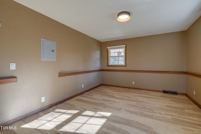 empty room with electric panel, visible vents, baseboards, and light wood-style flooring