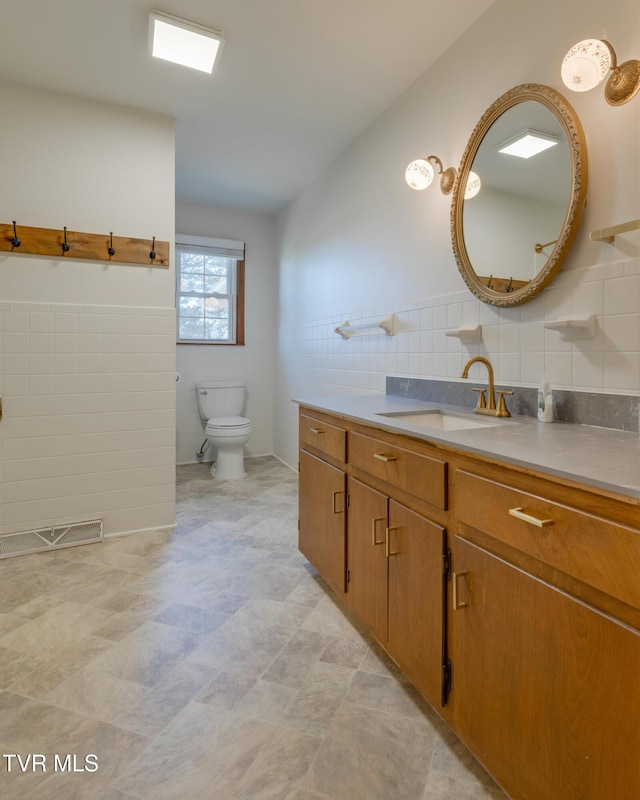 bathroom featuring visible vents, tile walls, a wainscoted wall, toilet, and vanity