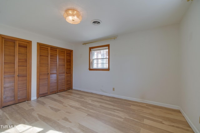 unfurnished bedroom featuring light wood-type flooring, visible vents, multiple closets, and baseboards