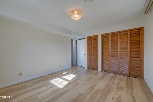 unfurnished bedroom with baseboards, multiple closets, and light wood-style flooring