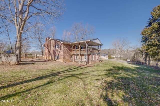 back of house with a balcony, fence, a chimney, a lawn, and brick siding