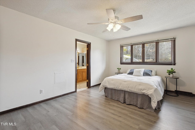 bedroom featuring baseboards, ensuite bath, light wood-style flooring, ceiling fan, and a textured ceiling