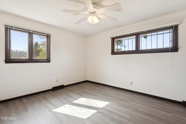 spare room featuring a ceiling fan, plenty of natural light, light wood-style floors, and baseboards