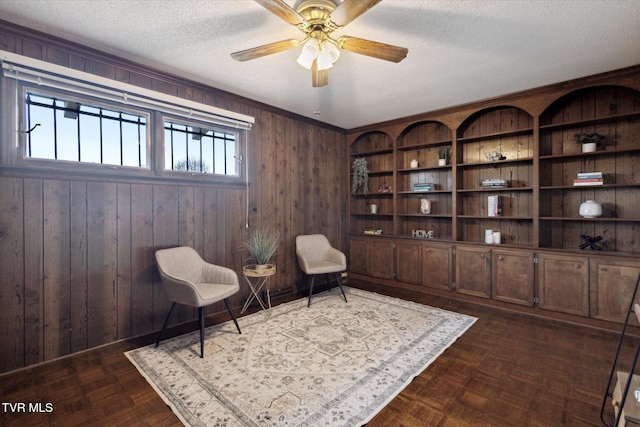 sitting room featuring wooden walls, a textured ceiling, and a ceiling fan