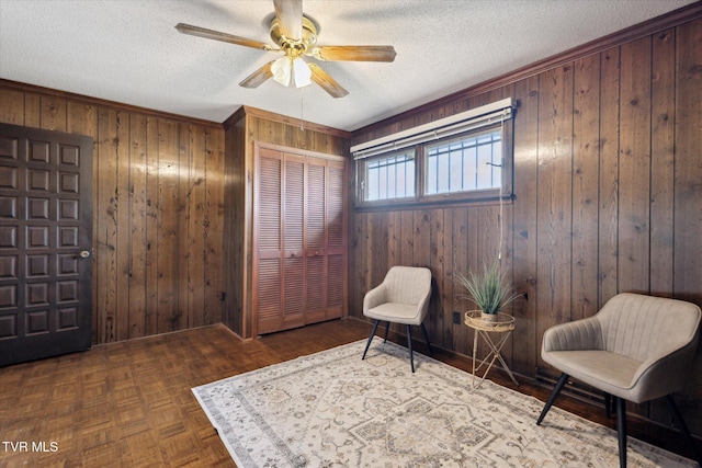 living area featuring ceiling fan, wooden walls, and a textured ceiling