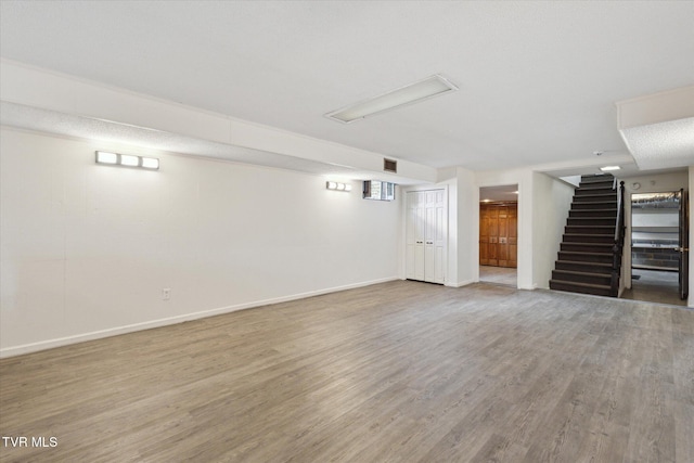 finished below grade area featuring stairway, baseboards, visible vents, and wood finished floors