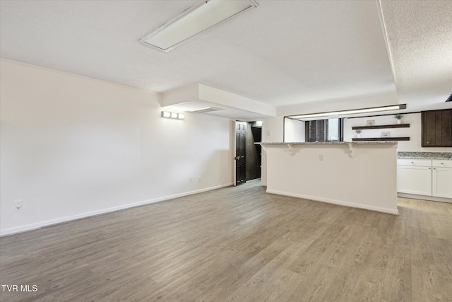 unfurnished living room featuring a textured ceiling, light wood-type flooring, and baseboards