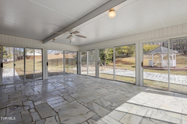 unfurnished sunroom featuring vaulted ceiling with beams, a wealth of natural light, and ceiling fan