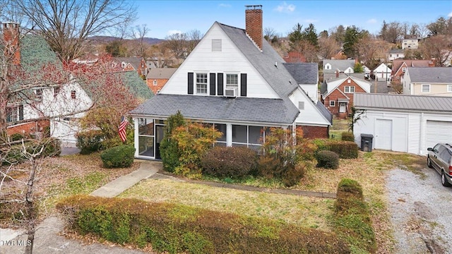 view of front of home featuring an outbuilding, a front lawn, roof with shingles, a sunroom, and a chimney