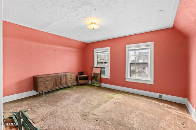 unfurnished room with carpet flooring, a textured ceiling, baseboards, and lofted ceiling