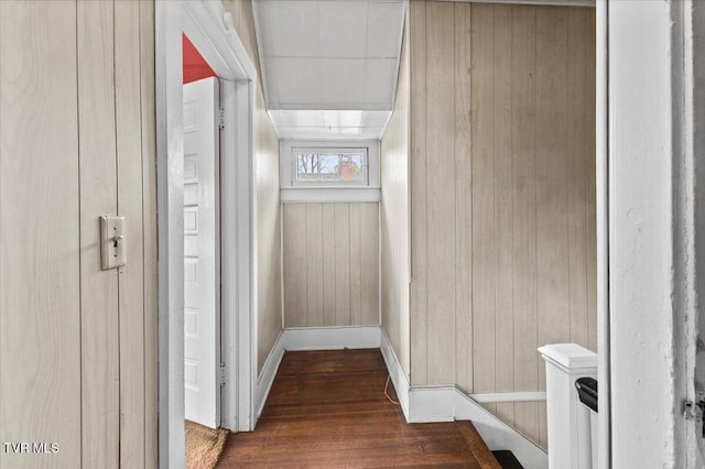 corridor featuring baseboards, wooden walls, and wood finished floors