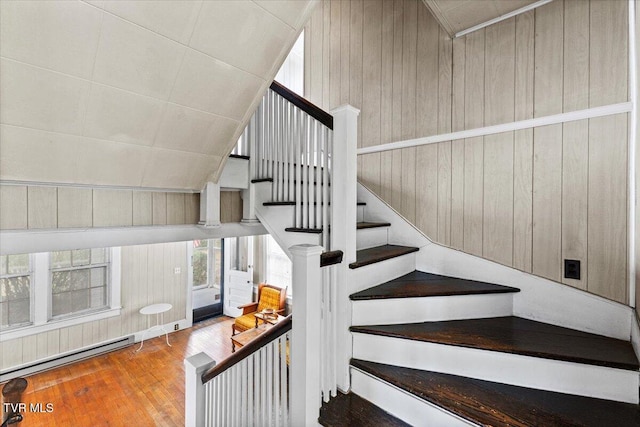 staircase with lofted ceiling, baseboard heating, wood finished floors, and wood walls