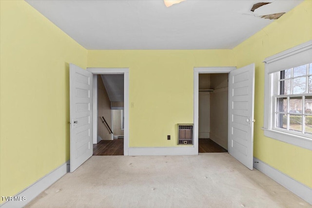 unfurnished bedroom with heating unit, carpet flooring, baseboards, and a closet