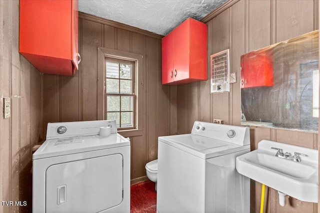 laundry area with wooden walls, washing machine and clothes dryer, laundry area, a sink, and a textured ceiling