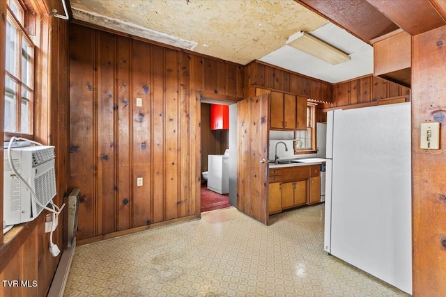 kitchen with light floors, washer / clothes dryer, freestanding refrigerator, a sink, and wood walls