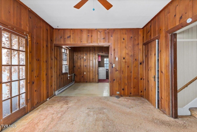 carpeted empty room with a baseboard heating unit, stairway, wood walls, cooling unit, and a ceiling fan