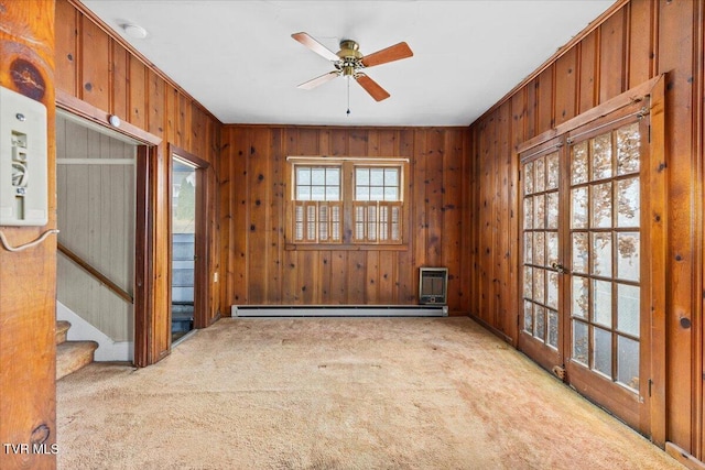 carpeted empty room with ceiling fan, a baseboard radiator, wood walls, and stairway