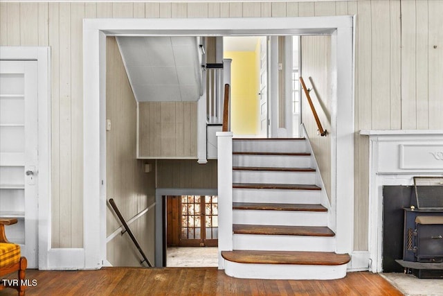 stairway with wooden walls, wood finished floors, and a wood stove