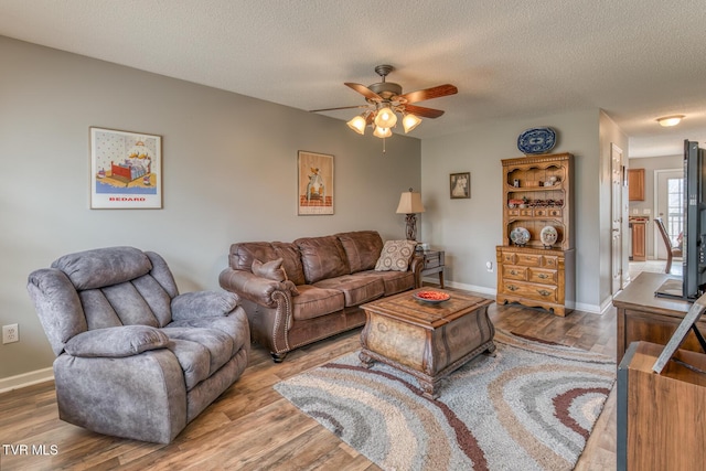 living area featuring ceiling fan, a textured ceiling, baseboards, and wood finished floors